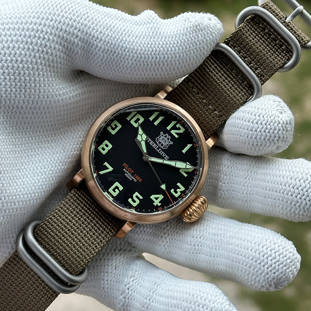 Steeldive SD1903S bronze pilot watch held in gloved hand, black dial with green numerals, wrist shot