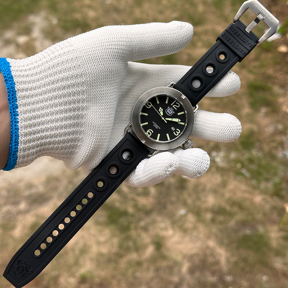 Steeldive SD1912 V2 brushed dive watch with black rubber strap held in white gloved hand outdoors