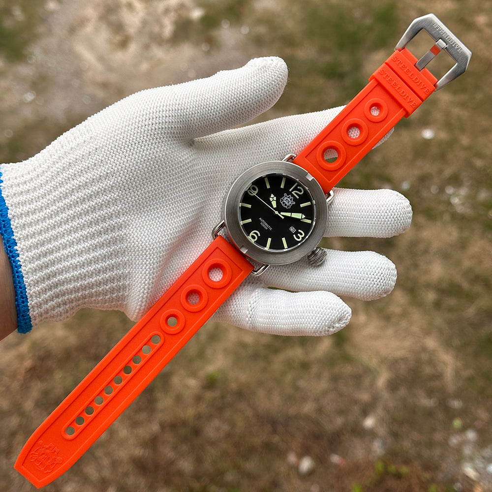 Steeldive SD1912 V2 brushed dive watch with bright orange rubber strap held in gloved hand outdoors