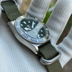 STEELDIVE SD1925 three-quarter view of the dark green dial and ceramic bezel on an army green nylon strap