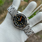 STEELDIVE SD1929V on a steel bracelet held in a gloved hand, black dial with orange minute hand