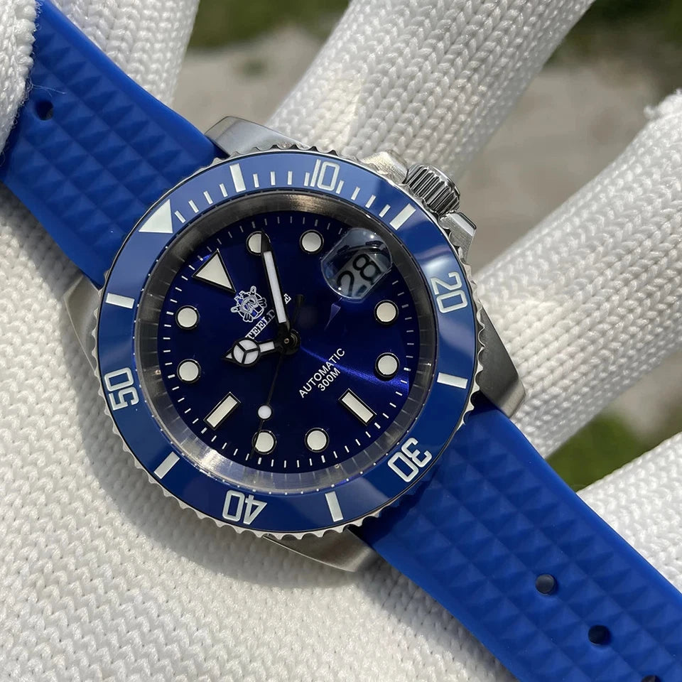 Steeldive SD1953 automatic diver watch with deep blue dial and bezel, luminous markers and date magnifier, blue rubber strap, stainless steel case and 300m water resistance, displayed on a white glove with blurred green background.