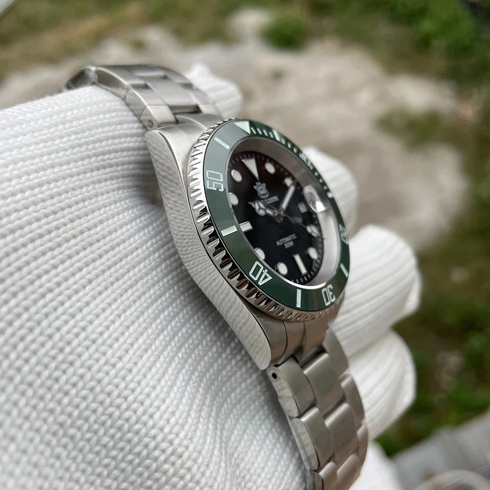 Angled view of Steeldive SD1953 automatic diver watch with black dial, green bezel and silver stainless steel bracelet held by a gloved hand against a blurred natural background.