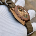 Steeldive SD1953S bronze dive watch with monochrome bezel and khaki NATO strap held on gloved hand