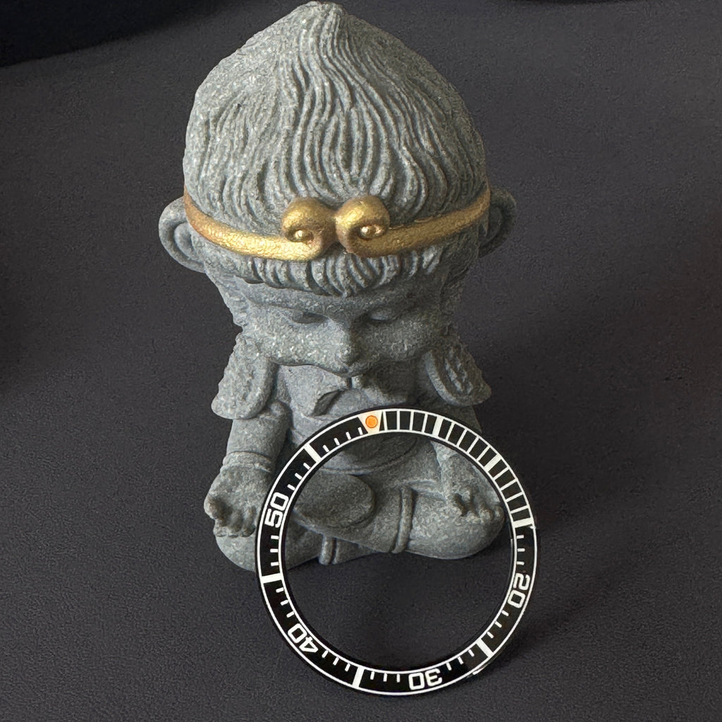 Steeldive SD1961 ceramic bezel insert leaning on stone figurine, white 60-minute scale and orange pip visible