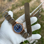 Steeldive SD1962S bronze dive watch on khaki zulu nato strap held in gloved hand, wrist-style view