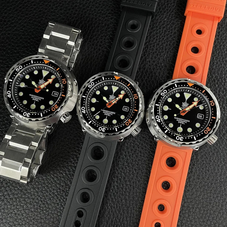 Three Steeldive SD1975C dive watches on textured black surface: one with stainless steel bracelet, one with black rubber strap, and one with orange rubber strap; black dials with orange accents, luminous markers, NH35 automatic movement.