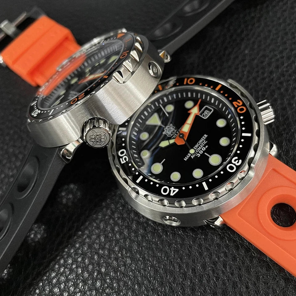 Side-by-side view of two Steeldive SD1975C dive watches on textured black surface, one with orange rubber strap and one with black rubber strap, stainless steel cases, black dials with orange accents, luminous markers.