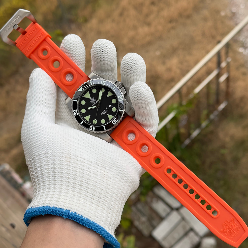 Steeldive SD1987 dive watch with orange perforated rubber strap held in gloved hand outdoors, lifestyle