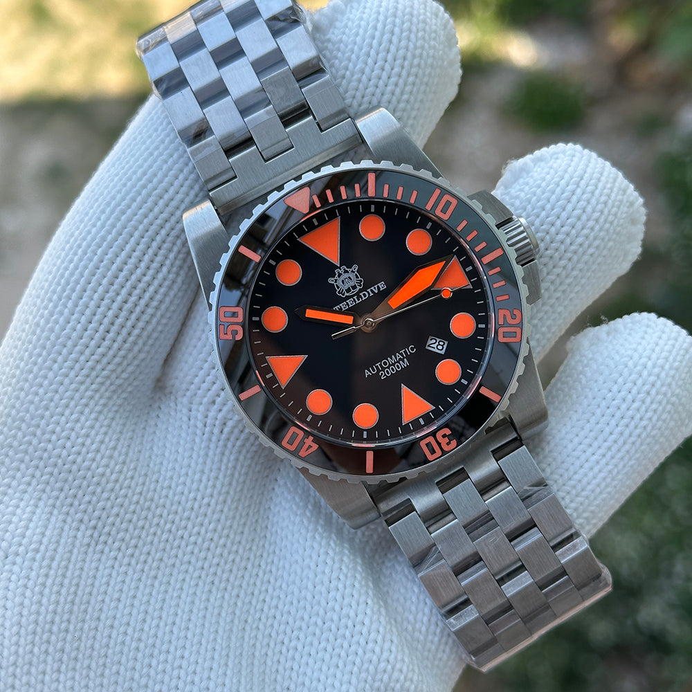 Steeldive SD1987 with orange-accented black dial on steel oyster bracelet shown in gloved hand