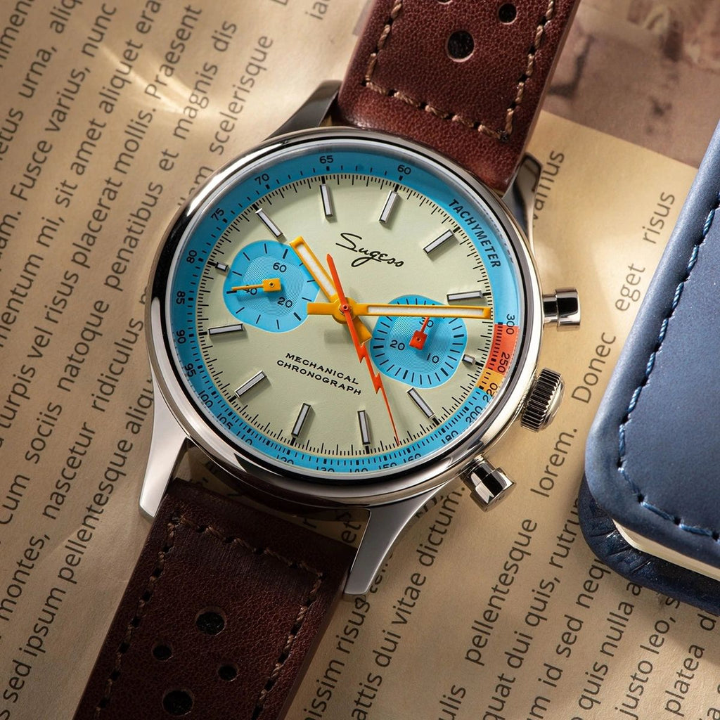 Sugess 387F teal-blue panda chronograph flat-lay on a printed page with brown leather strap