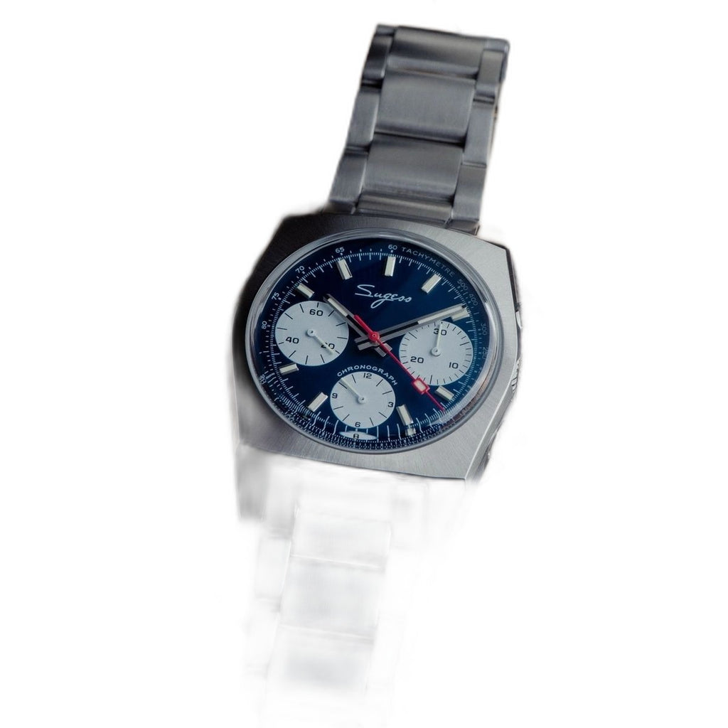 Sugess S419 blue dial, white sub-dials, steel bracelet, angled view beside a camera lens