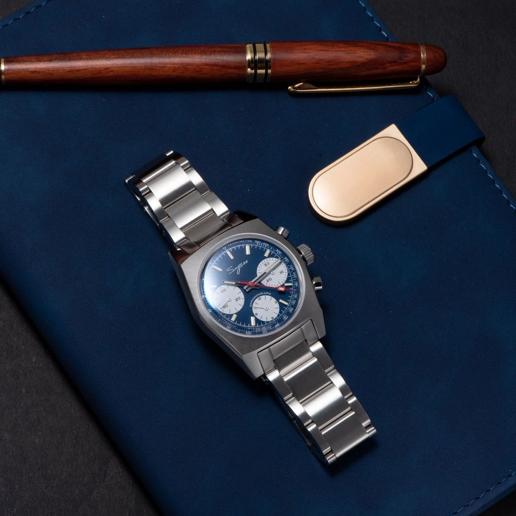 Sugess S419 blue dial, white sub-dials, steel bracelet, angled view resting on a blue book