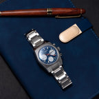 Sugess S419 blue dial, white sub-dials, steel bracelet, angled view resting on a blue book