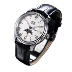 Sugess S437 silver dial moonphase, steel case, black leather strap, angled view beside a blue book