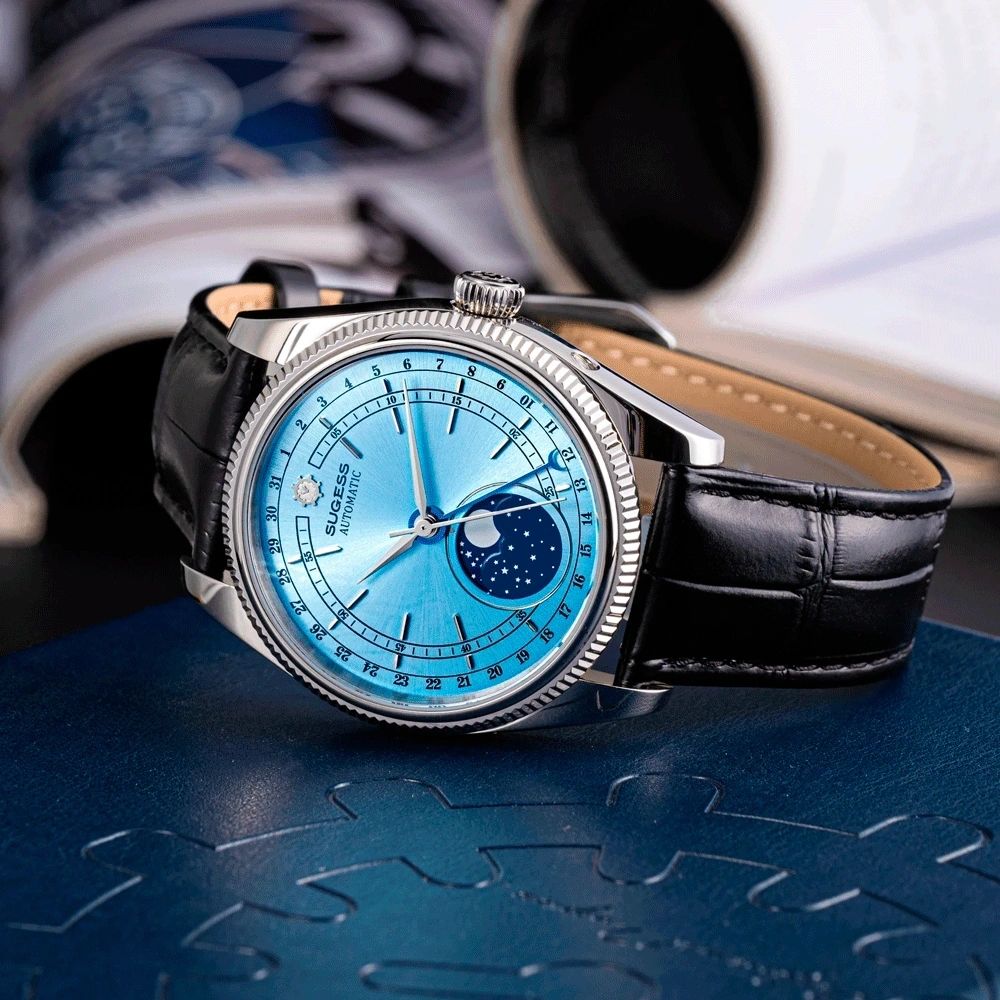 Sugess S452 steel moonphase watch, ice blue dial, black leather strap, angled view on a blue surface