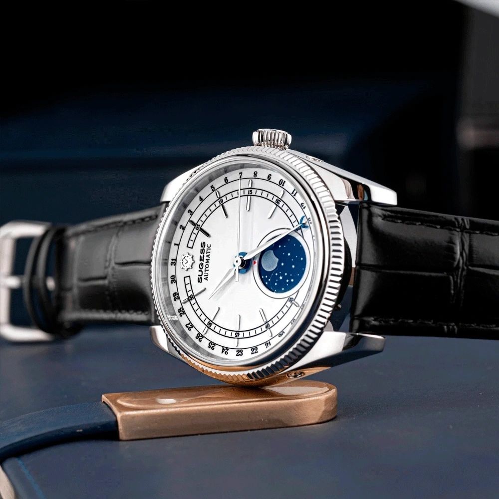 Sugess S452 steel moonphase watch, white dial, black leather strap, low side angle on a bronze stand, blue backdrop