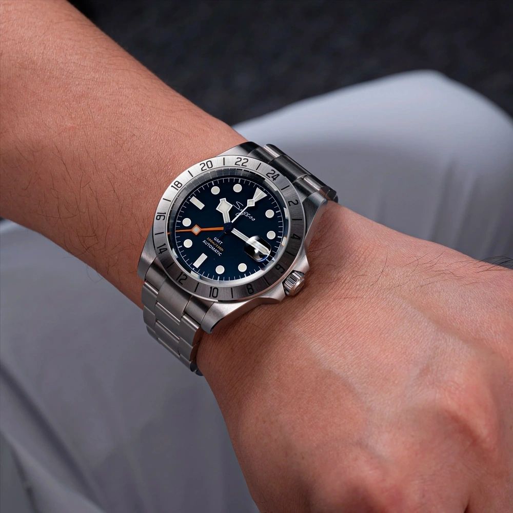 Sugess S463 GMT blue dial watch worn on the wrist with a white shirt cuff, steel bracelet