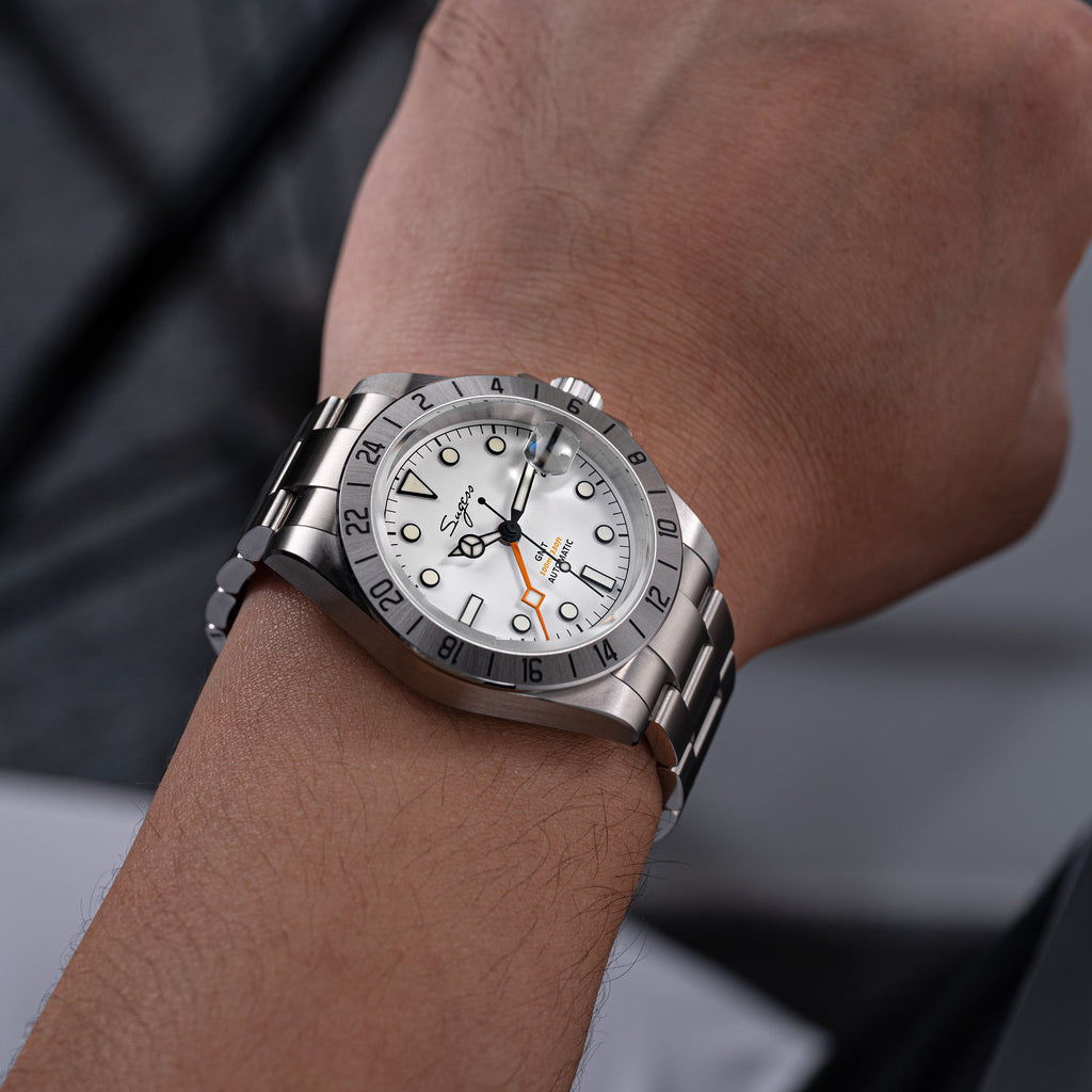 Sugess S463 white-dial GMT automatic watch worn on the wrist, steel bracelet, against a grey backdrop
